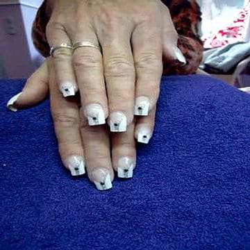 Lange weiße French-Nägel mit je einem schwarzen Punkt, Hand auf violettem Tuch