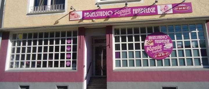Ladenfront: beerenfarbene Fassade mit großen Sprossenfenstern, darüber das Schild „Nagelstudio Rosis Nagelwelt Fusspflege“