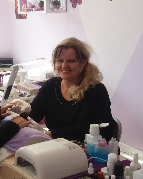 Rosi Rings lächelnd an ihrem Arbeitsplatz im Studio, vor ihr UV-Lampe und Pflegeprodukte