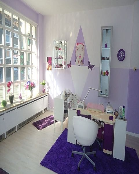 Rosis Behandlungsplatz: weißer Arbeitstisch mit UV-Lampen vor fliederfarbener Wand, violetter Teppich, Orchideen auf der Fensterbank