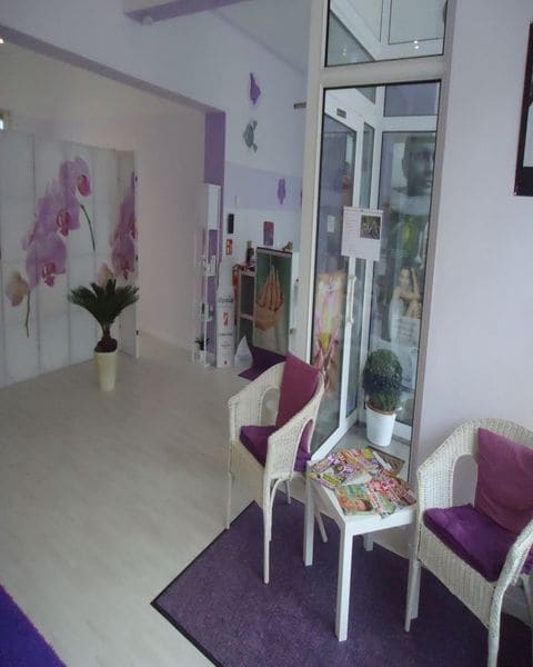 Wartebereich im Studio: zwei weiße Korbsessel mit violetten Kissen, Orchideen-Wandbild, Blick zur Eingangstür